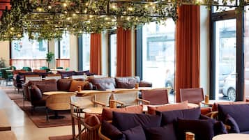 Un café moderno con mobiliario de mimbre, ventanas amplias y un techo decorado con plantas e iluminación.