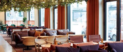 Un café moderno con mobiliario de mimbre, ventanas amplias y un techo decorado con plantas e iluminación.