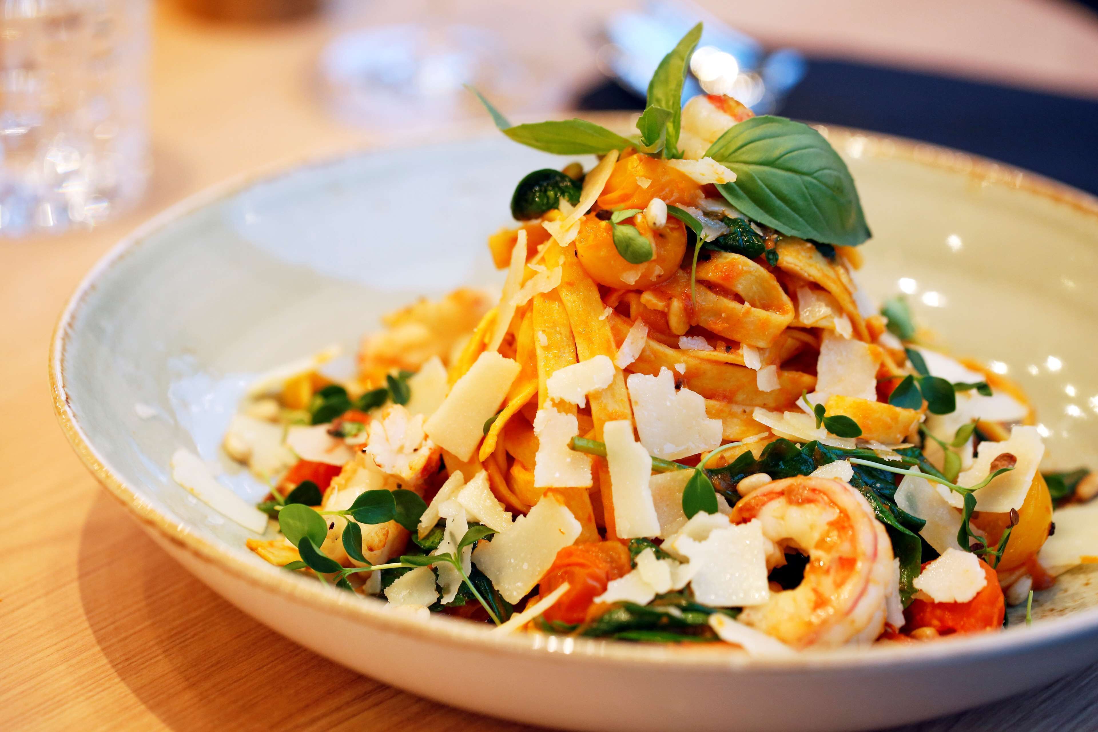 A plate of pasta with shrimp, cheese, and greens.