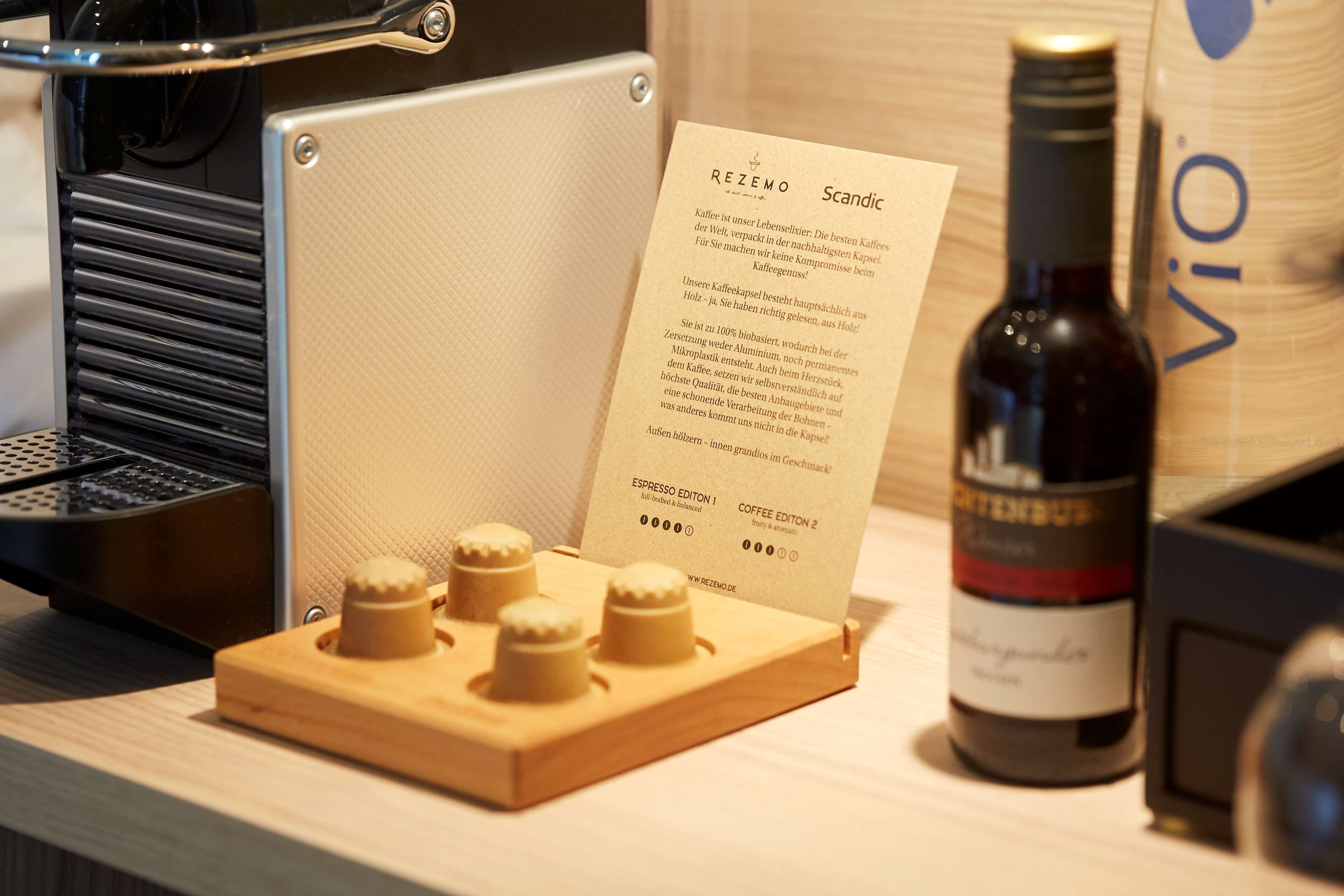 Uma máquina de café, uma prensa de madeira para café, uma garrafa de vinho e um menu sobre a mesa.