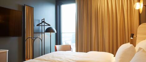 Una habitación de hotel con una cama grande, una silla, un escritorio, una lámpara y un ventanal con cortinas.