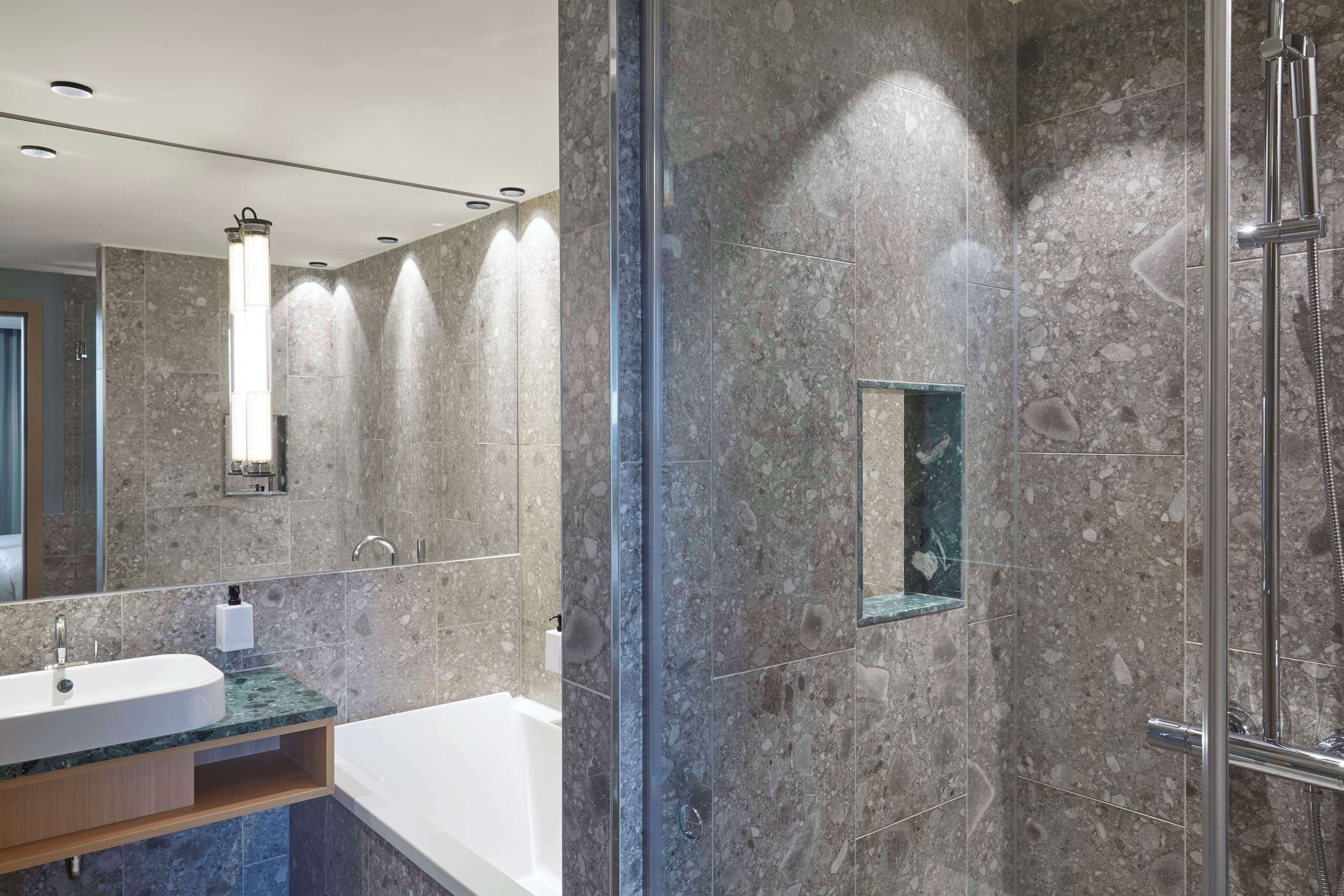 Un baño moderno con lavamanos de mármol, ducha con cerramiento de vidrio y espejo integrado.