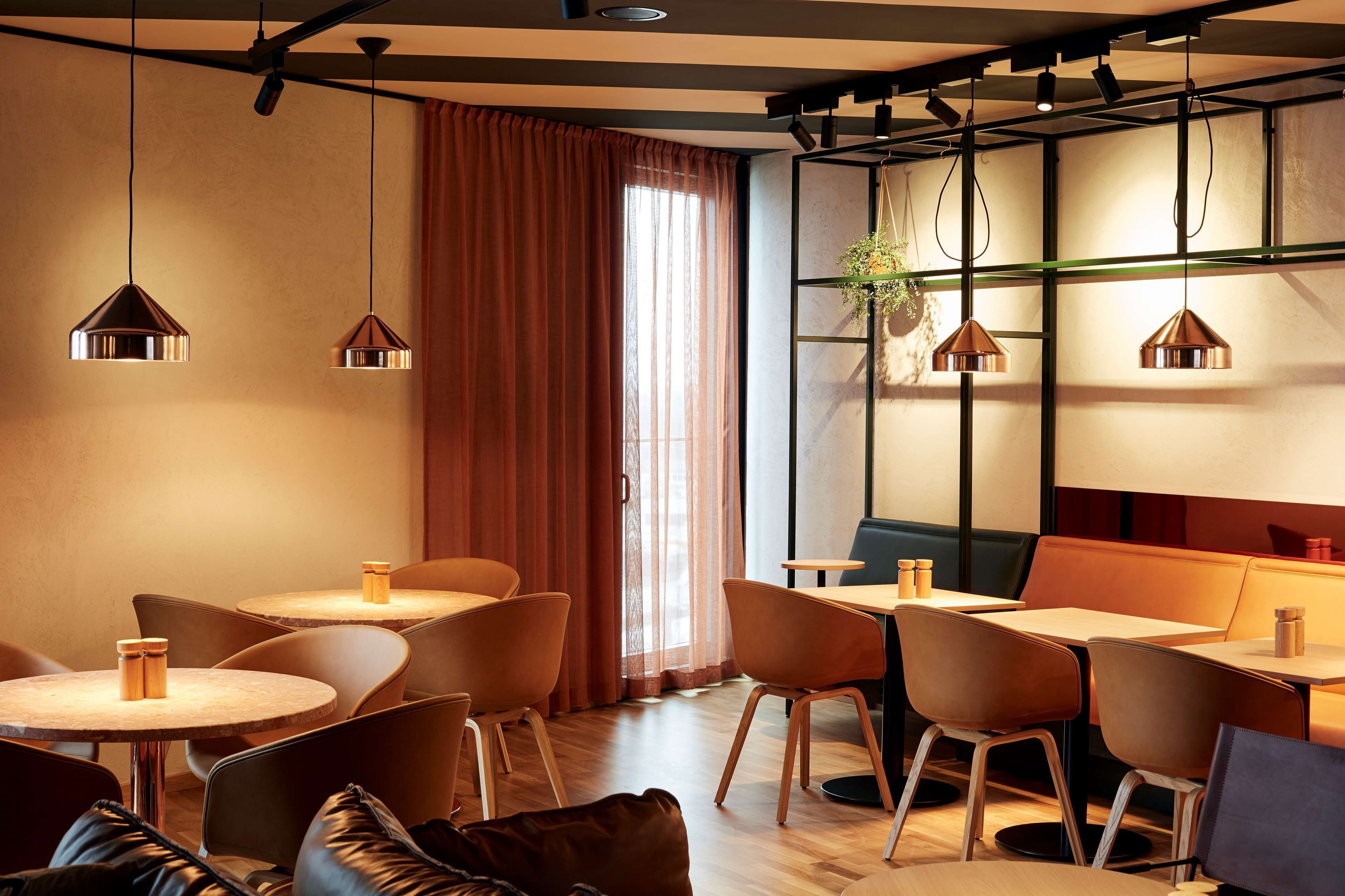 A modern interior with round tables and chairs, pendant lighting, and a large window with curtains.