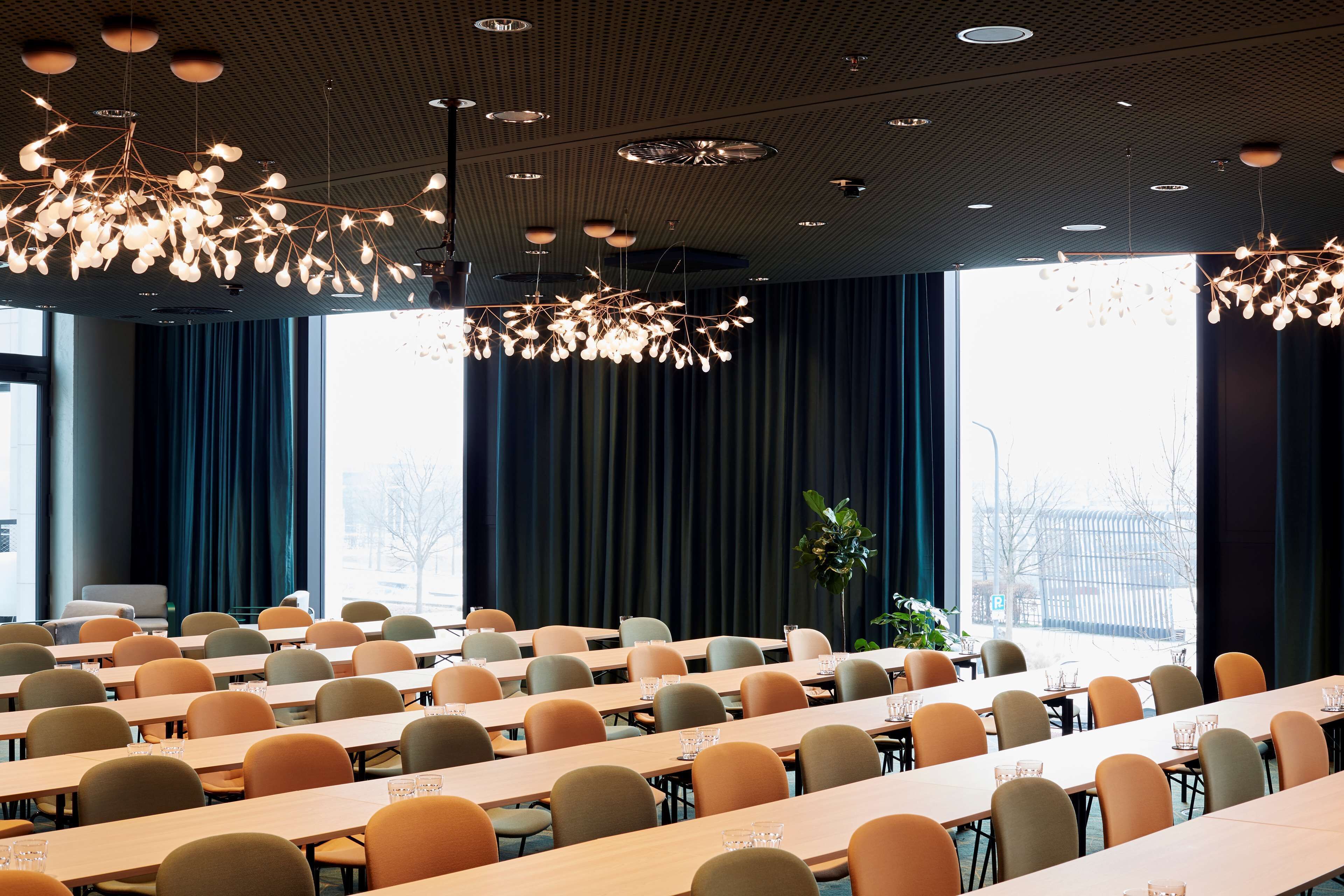 A conference room with multiple tables and chairs, large windows, and a modern chandelier.