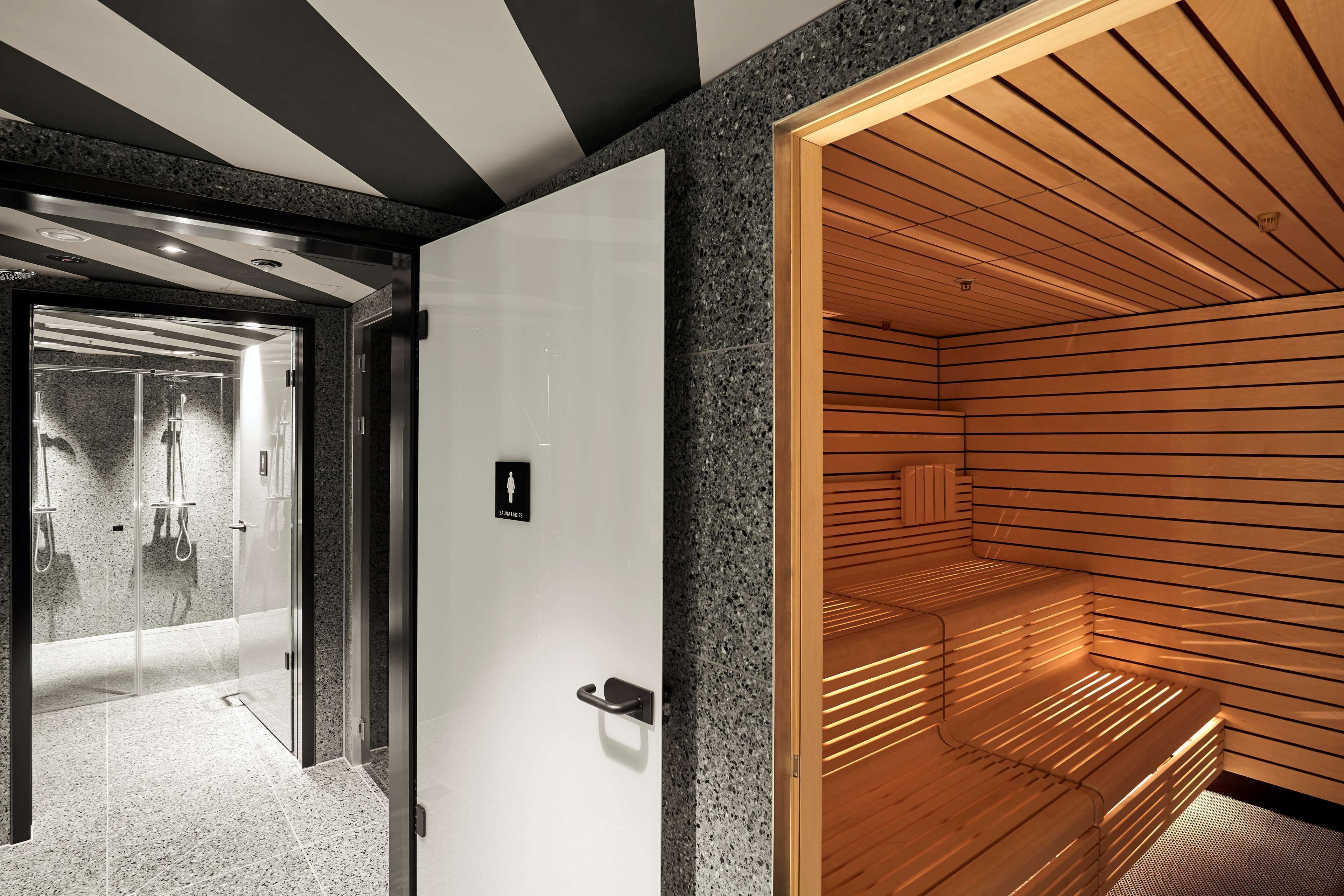 Un intérieur moderne avec un sauna, une douche à l’italienne entourée de parois de verre et un banc en bois.