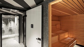 Un intérieur moderne avec un sauna, une douche à l’italienne entourée de parois de verre et un banc en bois.