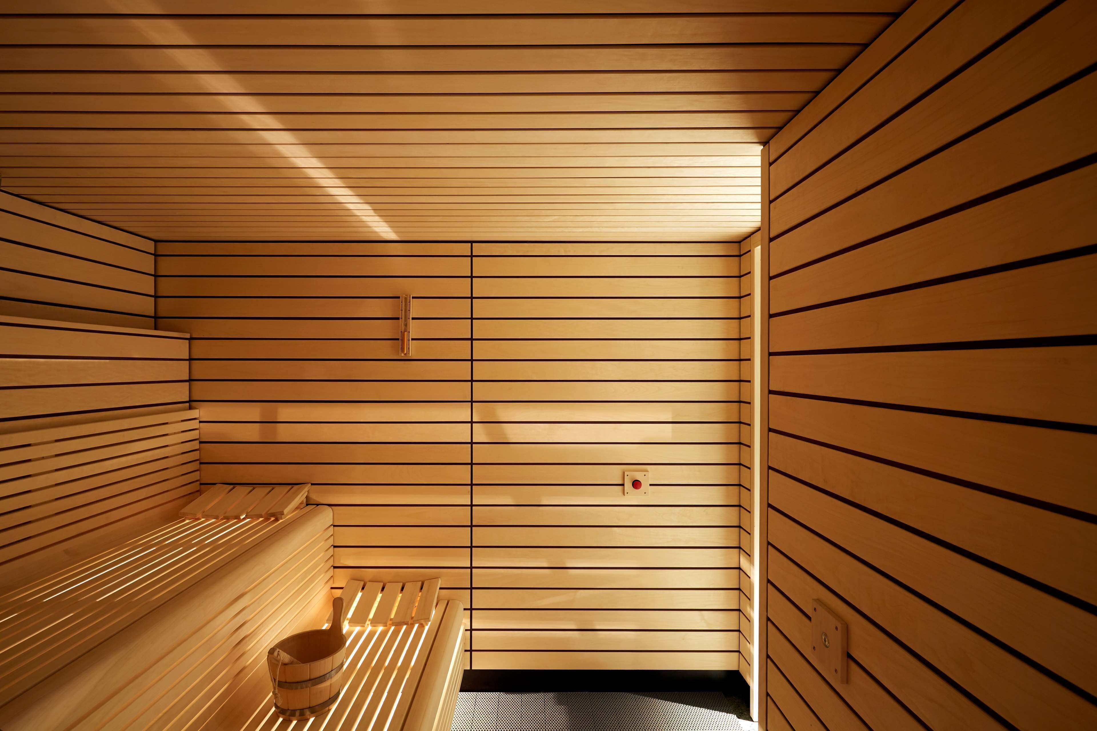 A sauna room with wooden slats, benches, and a bucket.