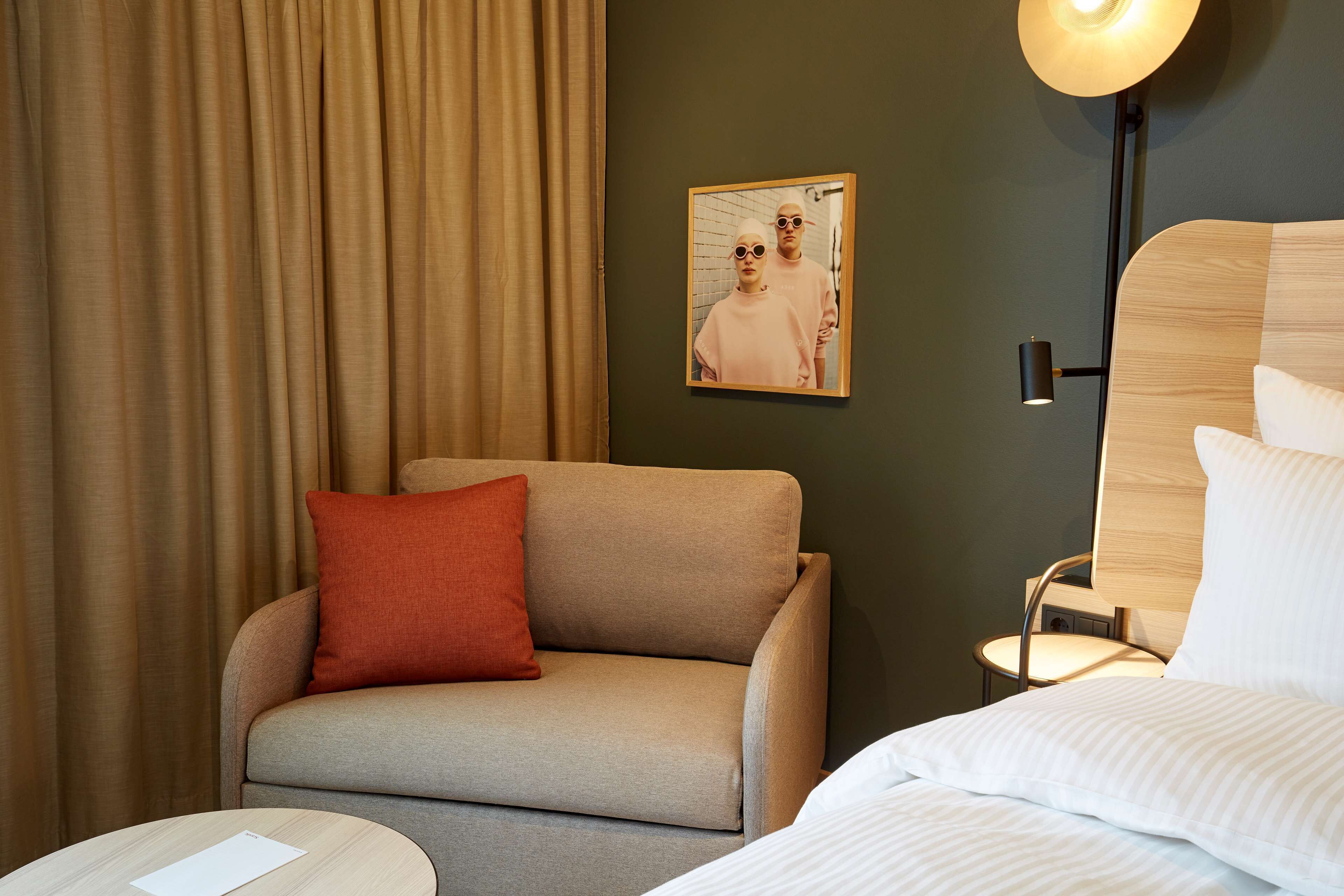 A hotel room with a sofa, a small table, a bed, a lamp, and a framed picture on the wall.