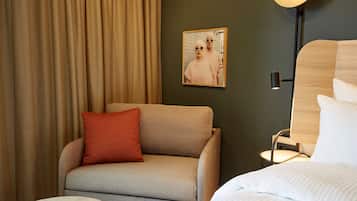 A hotel room with a sofa, a small table, a bed, a lamp, and a framed picture on the wall.