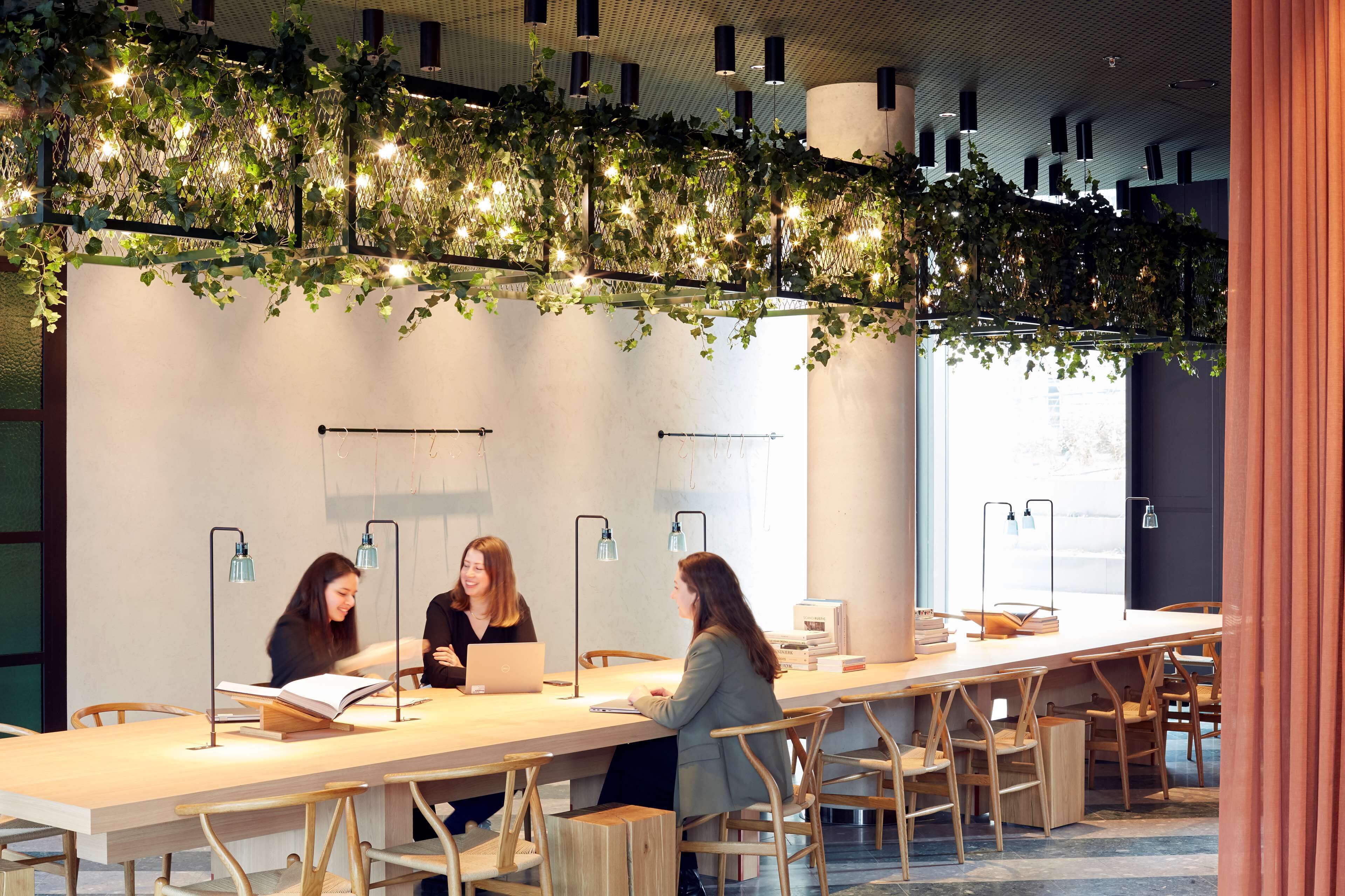 A modern indoor space with a long table, chairs, and three people engaged in a discussion.