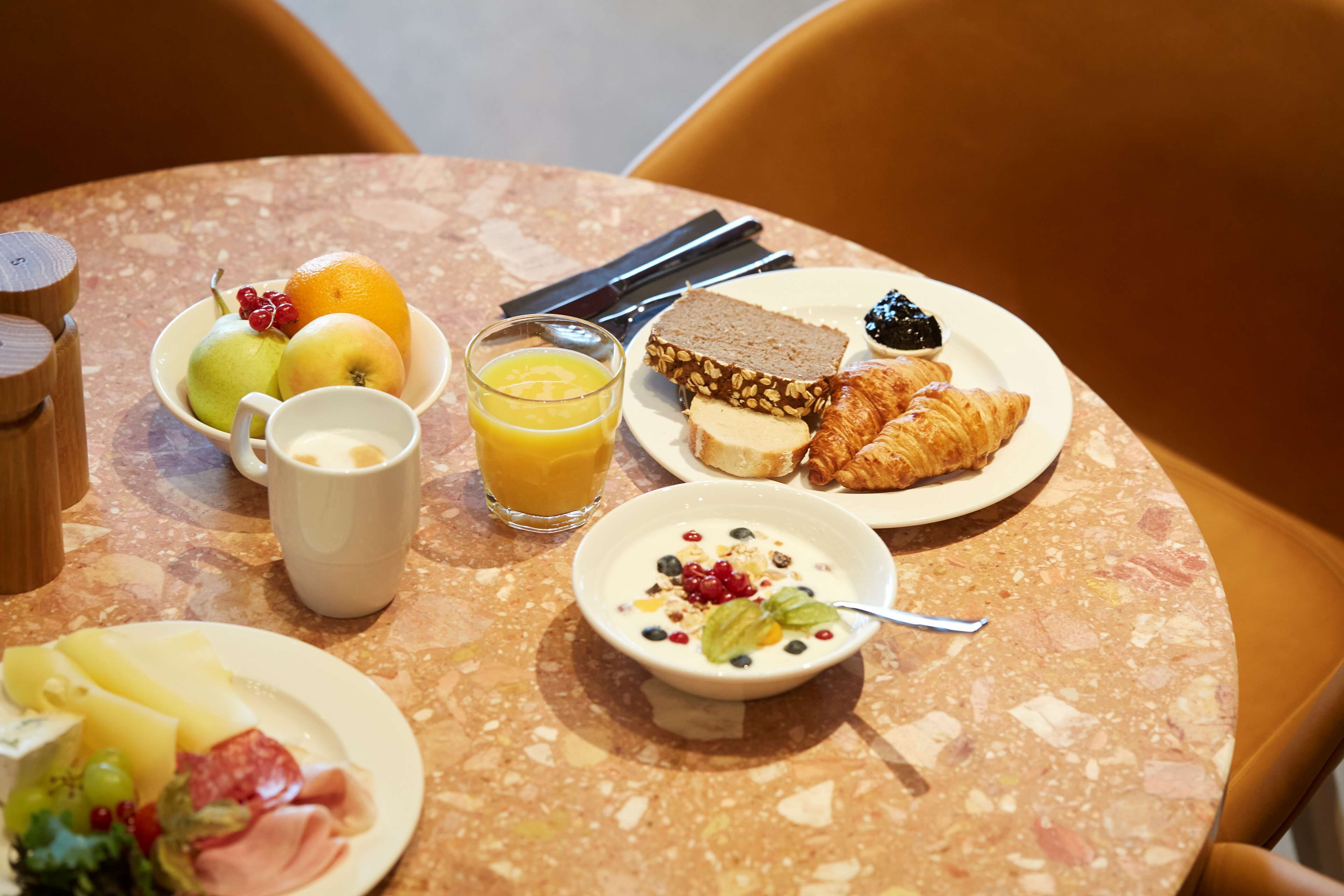 A breakfast table with plates of food, a glass of orange juice, and a bowl of yogurt.