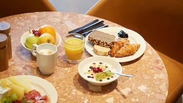 A breakfast table with plates of food, a glass of orange juice, and a bowl of yogurt.