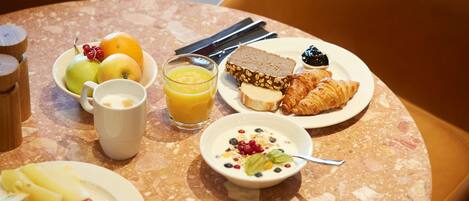 A breakfast table with plates of food, a glass of orange juice, and a bowl of yogurt.
