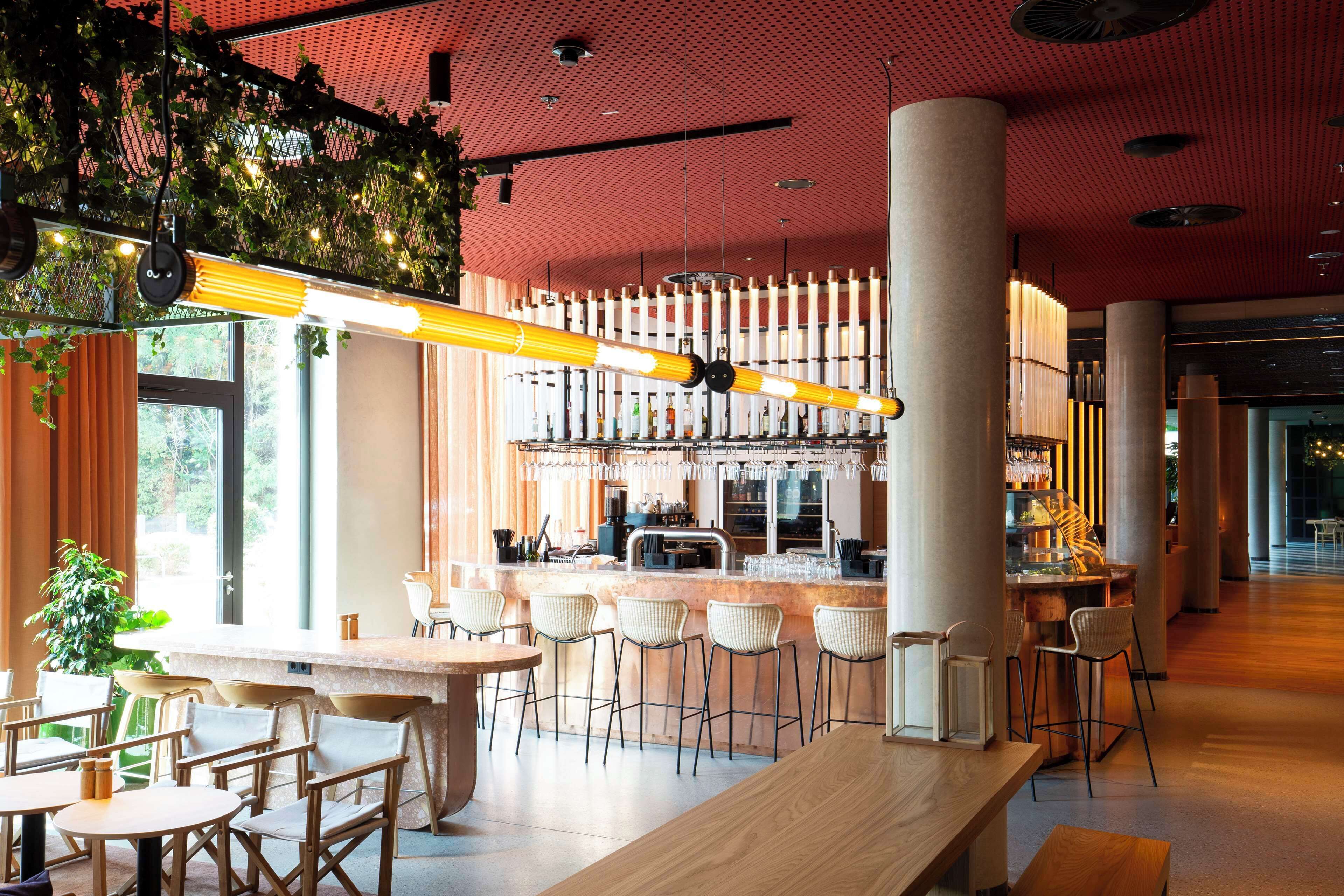 A modern bar area with a long counter, bar stools, and a seating area with tables and chairs.