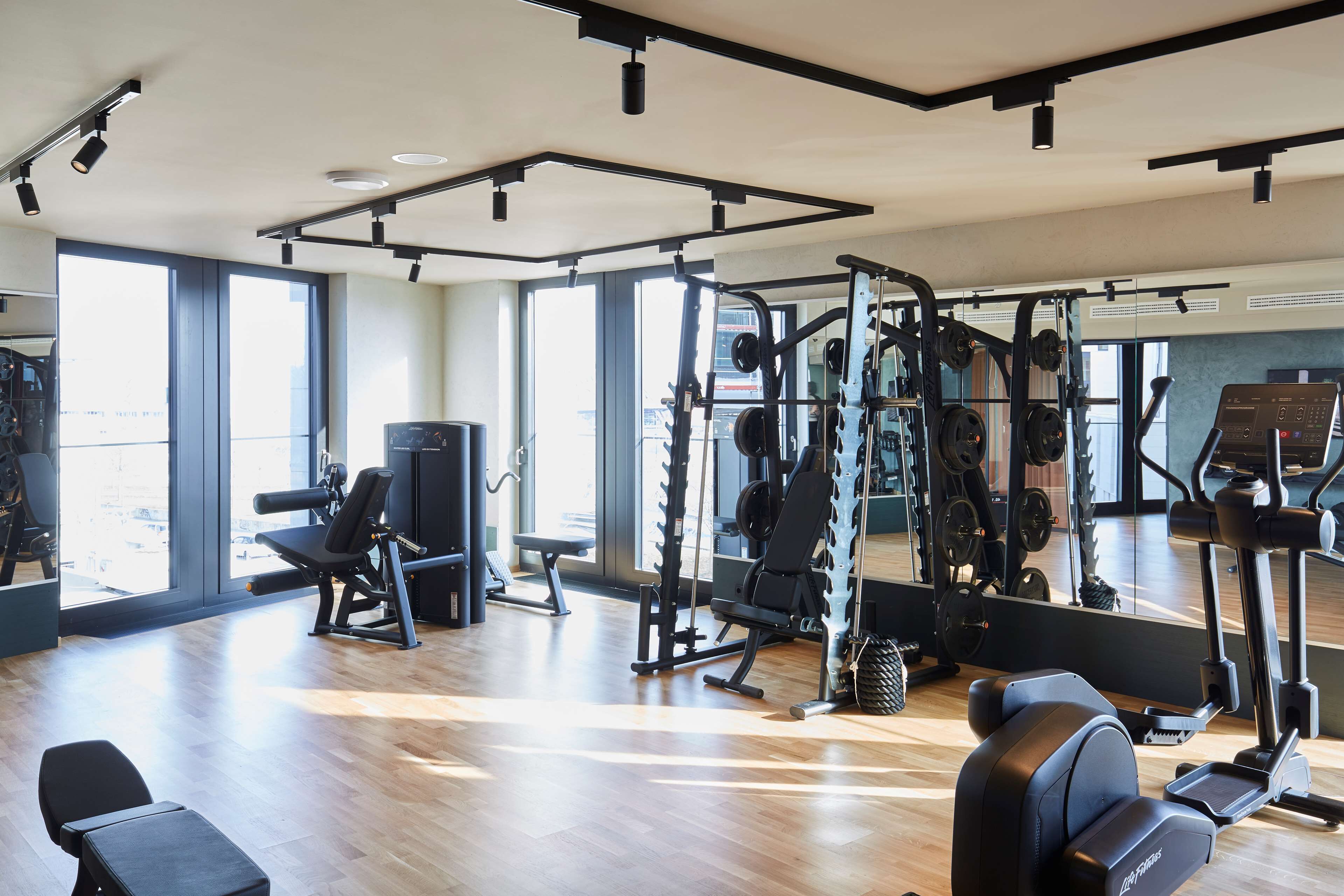 Un gimnasio moderno con diverso equipo de ejercicio, amplias ventanas y suelo de madera.