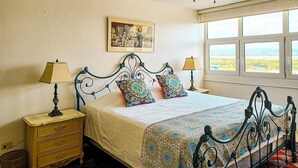 Een slaapkamer met een bed, twee nachtkastjes, een raam met uitzicht en een ingelijste foto aan de muur.