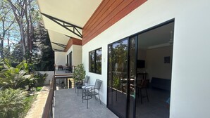 Un patio exterior moderno con zona de comedor, entrada por puerta de cristal y vistas al entorno verde.