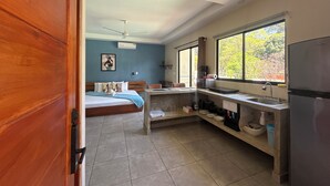 Una habitación con cama, una kitchenette pequeña, una ventana con vistas y un ventilador de techo.