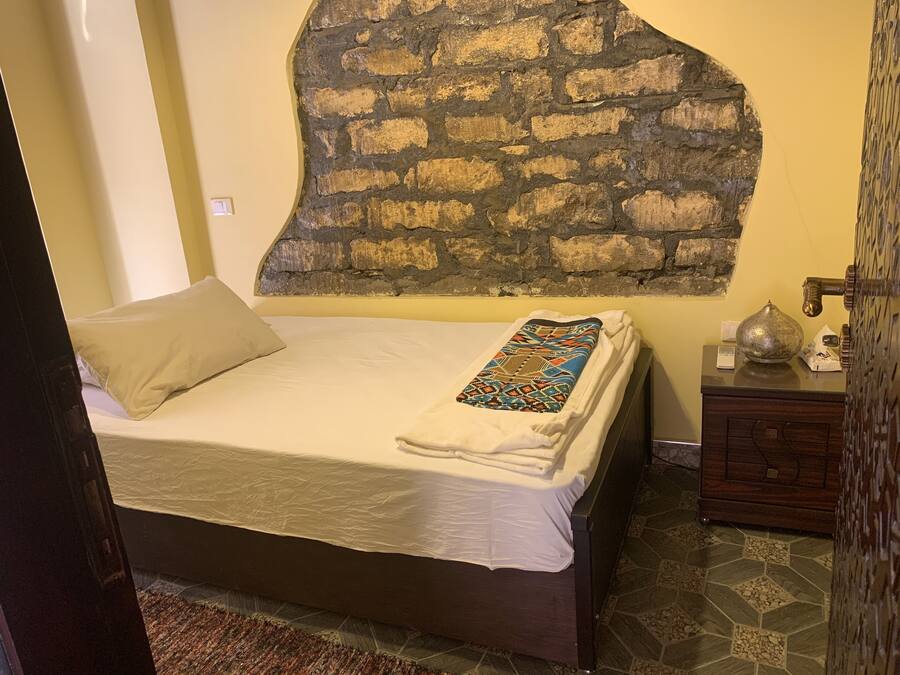 A neatly made bed with a patterned throw, a bedside table with a decorative item, and a stone wall.