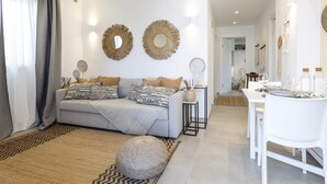 A modern living room with a grey sofa, patterned cushions, a woven rug, and a dining area with a white table and chairs.