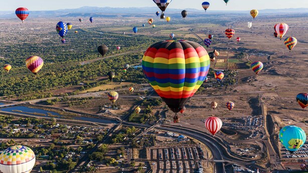 Un grand nombre de montgolfières survolent une ville, avec ses rues et ses bâtiments.
