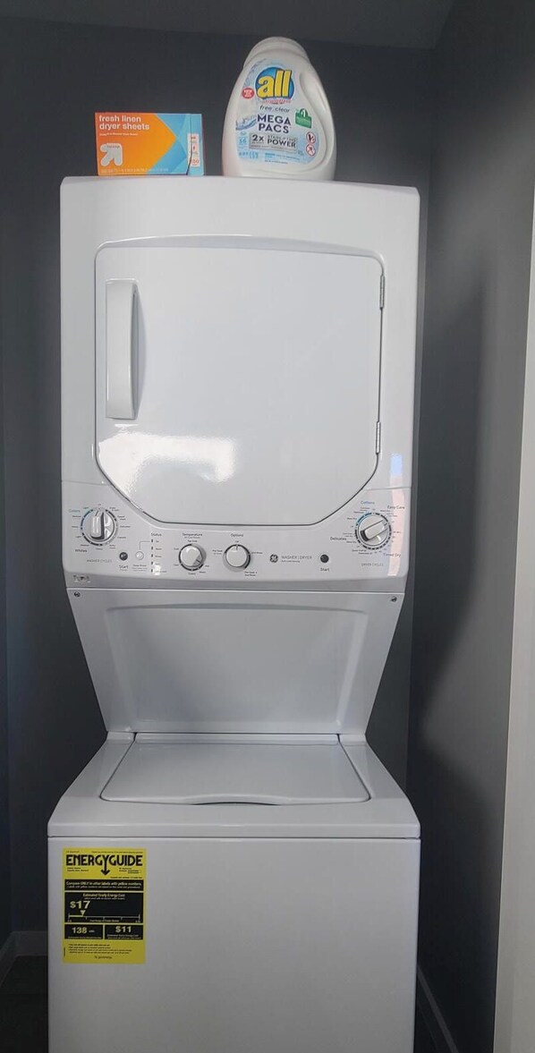 Une vue de face d’un lave-linge à chargement frontal blanc, avec un panneau de commande, une bouteille de lessive et une boîte de feuilles d’adoucissant pour le sèche-linge.