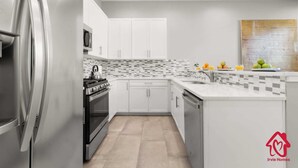 Uma cozinha moderna com armários brancos, painel de azulejos, geladeira de aço inoxidável e uma pia.