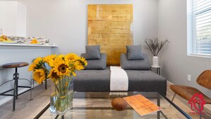 Uma sala de estar moderna com um sofá cinza, uma mesa de centro de vidro e um vaso de girassóis.