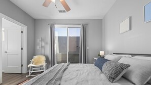 Une chambre à coucher avec un lit, une chaise, une table de chevet et une fenêtre avec des rideaux.