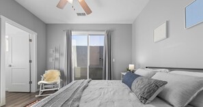 A bedroom with a bed, a chair, a nightstand, and a window with curtains. - Downtown Luxury Townhouse w/Garage & Walkable (Albuquerque)