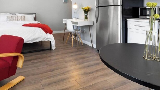 Ein modernes Hotelzimmer mit einem Bett, einem roten Sessel, einem kleinen Tisch und einer Küchenzeile.