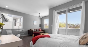 Een moderne slaapkamer met een groot bed, een bureau, een stoel, een bank en een plafondventilator.
