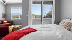 Ein Schlafzimmer mit einem großen Bett, einer roten Tagesdecke, einem braunen Ledersofa und einem Fenster mit Jalousien.