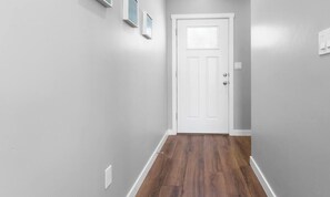 A hallway with a white door, grey walls, and wooden flooring. - Terrific Tijeras Getaway w Garage – An Irvie Home (Albuquerque)