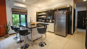 A modern kitchen with a central island, bar stools, stainless steel appliances, and a window with a view of greenery. - Resona Pool Villa by Aonanta Group (Krabi)