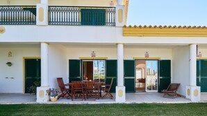 A two-story building with a covered outdoor seating area featuring wooden furniture and a potted plant. - Apartment Diana with pool (Albufeira)