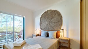 A bedroom with a large bed, a round wall hanging, and a view of the outdoors. - Apartment Diana with pool (Albufeira)