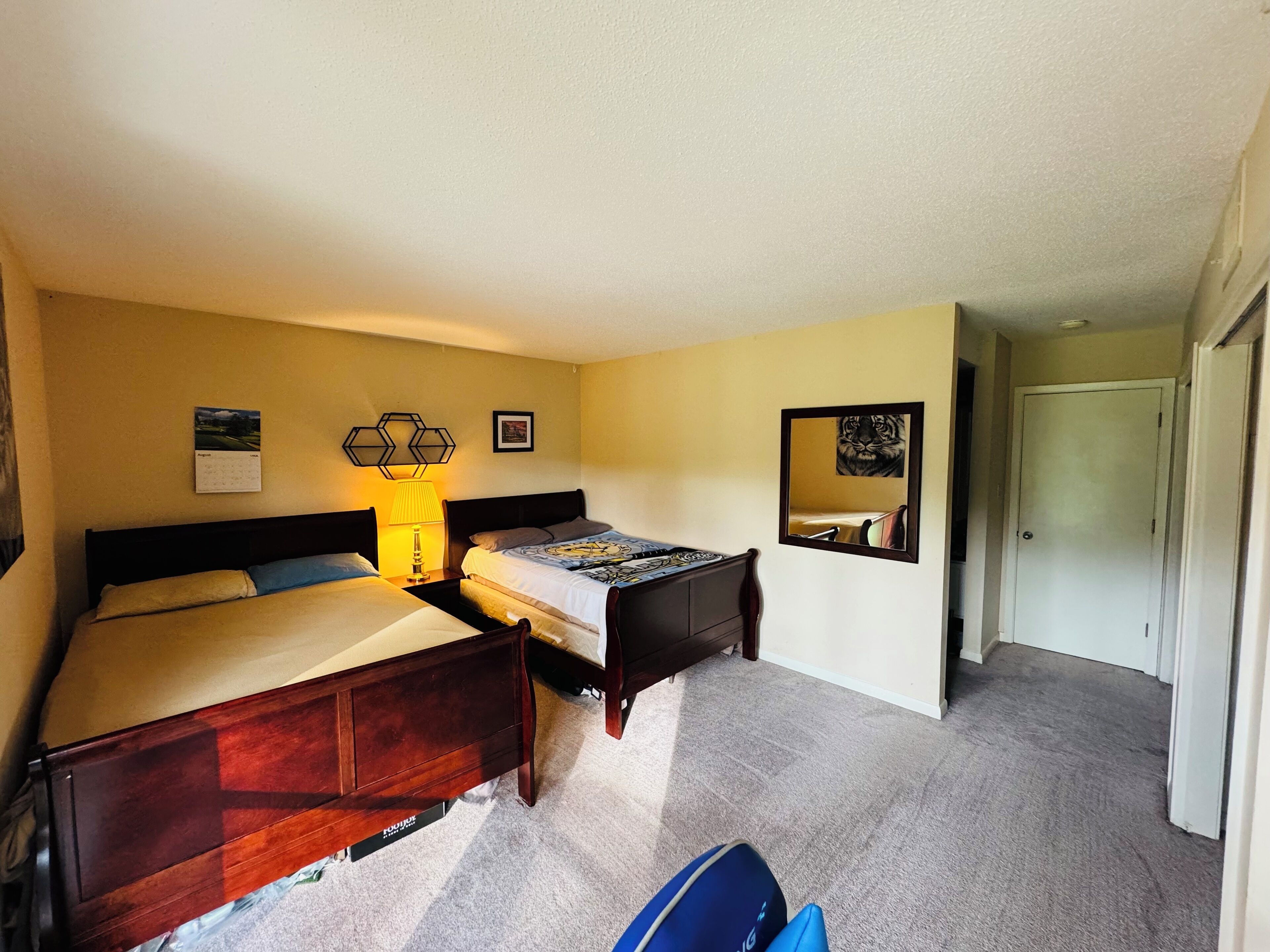 A hotel room with a bed, a desk, a lamp, a calendar, and a mirror.
