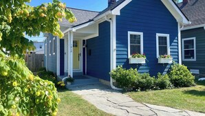 A blue house with a white porch, a stone pathway, and a small garden with bushes and a tree. - The Little Blue Cottage in Fountain Sq | Walkable! (Indianapolis)