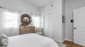 A bedroom with a bed, a dresser, a chair, a mirror, and a door. - The Little Blue Cottage in Fountain Sq | Walkable! (Indianapolis)