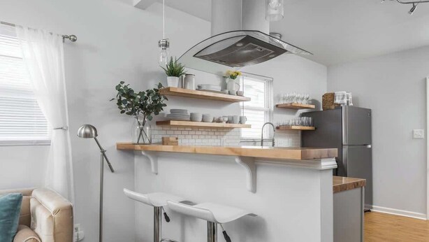 A modern kitchen with a central island, bar stools, and a built-in stove. - The Little Blue Cottage in Fountain Sq | Walkable! (Indianapolis)