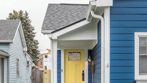 A residential house with a yellow front door, a blue exterior, and a small garden with stepping stones leading to the entrance. - The Little Blue Cottage in Fountain Sq | Walkable! (Indianapolis)