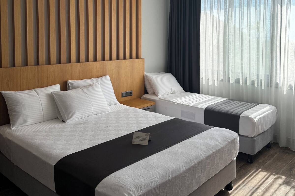 A modern hotel room with two beds, a wooden headboard, a ceiling light, and a window with curtains.