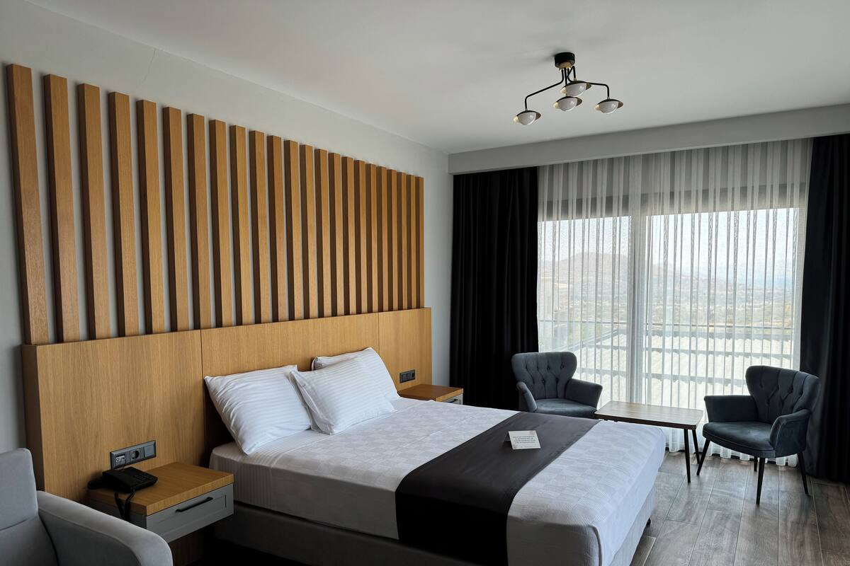 A modern hotel room with a large bed, two bedside tables, a desk, and a chair.
