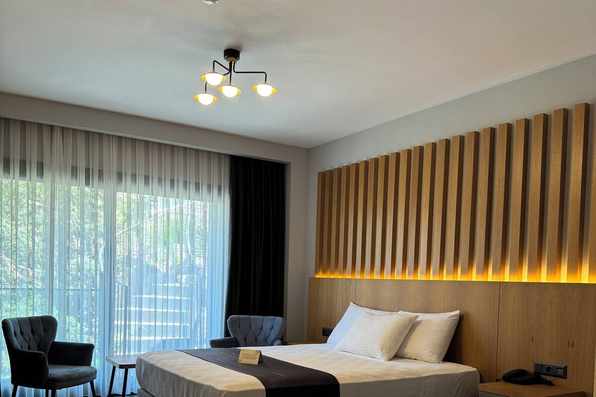 A hotel room with two beds, a desk, a chair, and a large window with curtains.