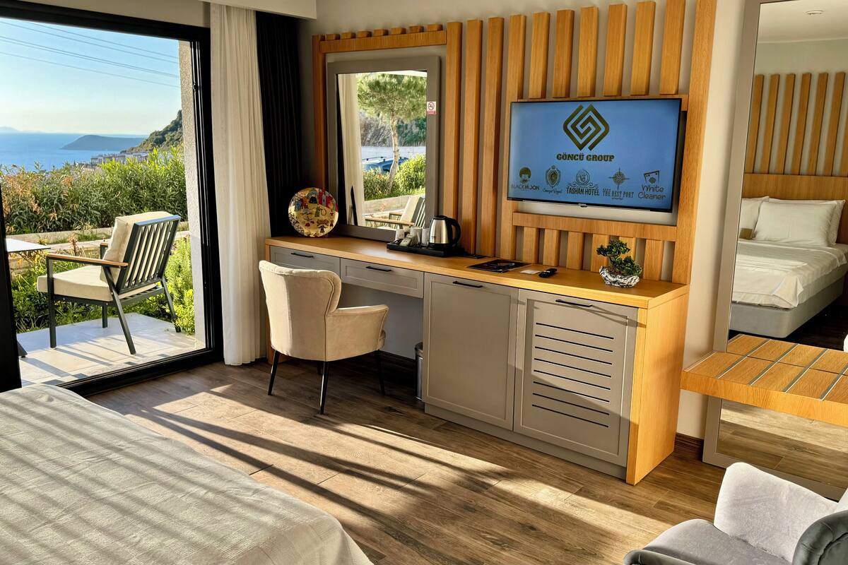 A hotel room with a bed, a desk with a computer, a TV, and a view of the sea.