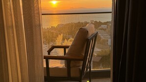 En balkong med en stol, gardiner och utsikt över solnedgången över vattnet.