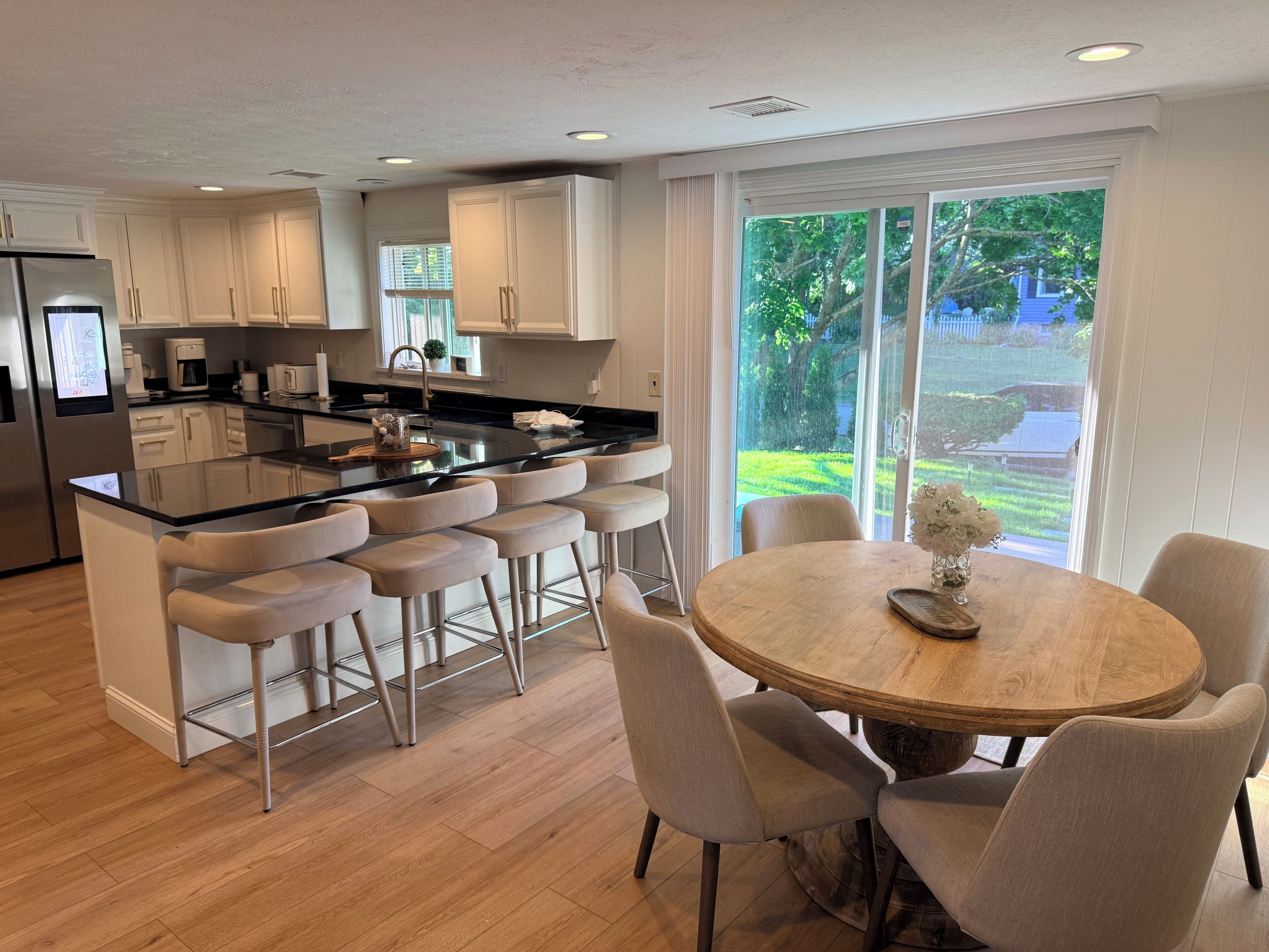 A modern kitchen with white cabinets, a central island with bar stools, and a dining table with chairs.