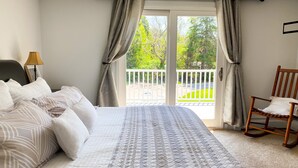 Una camera da letto con un letto, una sedia, una lampada e un balcone vista verde.