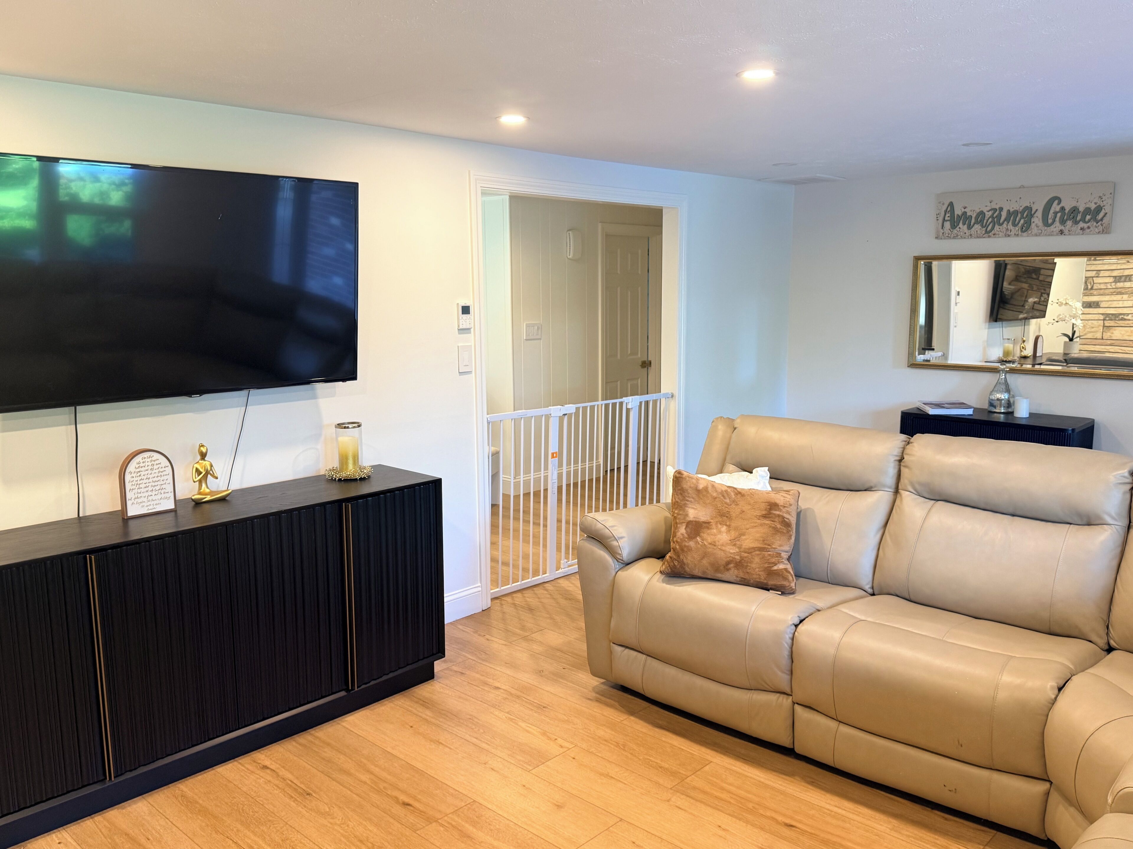 A living room with a flat-screen TV, a dark wood console, a beige leather sofa, and a small table with a mirror and decorative items.